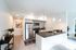 Open plan kitchen area with fridge, microwave, oven, countertops, and white walls.