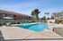 Pool with lounge chairs, sun, bushes, and table and chair sets
