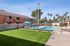 Pool with lounge chairs, sun, bushes, grass, and table and chair sets