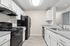 galley view of kitchen in B1 renovated floorplan at Timber Flats white cabinets black appliances and grey countertops