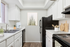 Virtually staged kitchen at Bridge Lane with black appliances, grey counters and brown flooring, coffee maker, cutting boards and kitchen utensils