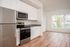 One Bedroom at Lyra Apartments - view from kitchen into the living room with stainless steel appliances and hardwood floors