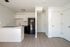 Kitchen and living area with fridge, counters, sink, cupboards, wooden floors, and doors.