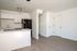 Kitchen and living area with fridge, counters, sink, cupboards, wooden floors, and doors.