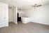 Open plan kitchen and living area with wooden floors, ceiling fan, doors, counters, cupboards, fridge, oven, and sink.