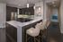 Elegant modern kitchen with sleek dark cabinetry, stainless steel appliances, and a stylish breakfast bar with soft beige chairs.