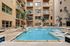 Luxurious apartment complex featuring a pristine swimming pool, chic lounge areas, and elegant balconies nestled among palm trees.