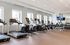 Spacious apartment gym with modern cardio equipment, bright windows, and flat-screen TV.