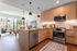 Modern open-concept kitchen and living area with sleek wood cabinetry, stainless steel appliances, and large windows overlooking lush greenery.