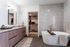 Luxurious bathroom featuring a modern freestanding tub, dual-sink vanity with sleek cabinetry, and a walk-in closet.