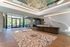 Elegant apartment lobby with luxurious patterned rug, artistic wall feature, and modern glass door entrance, flooded with natural light and outdoor views.