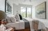 Bright and serene bedroom featuring a cozy bed with elegant pillows, modern art on white walls, and a large window with lush greenery views.