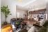 Contemporary open-plan living room with elegant decor, cozy seating, stylish pendant lights, and a modern kitchen featuring wood cabinets and stainless steel appliances.