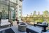 Chic apartment balcony with modern seating, overlooking lush green landscape through expansive glass doors, creating a serene and stylish outdoor living space.