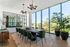 Elegant dining room with a sleek black table, plush green chairs, and floor-to-ceiling windows offering a scenic view of lush greenery.