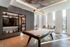 Modern apartment recreation room featuring a sleek billiards table, contemporary bookshelf with decor, and ample natural light through tall windows.