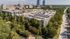 Aerial view of a modern apartment complex surrounded by lush greenery, with city skyline in the background, offering urban living amidst nature.