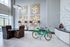 Elegant modern living area featuring chic dining set, stylish artwork, and a whimsical green bicycle, flooded with natural light from large windows.
