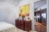 Inviting bedroom with elegant wooden dresser, cozy decor, and a peek into a modern kitchen with stainless steel appliances.