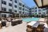 Pool courtyard with lounge seating, grilling stations, shaded dining table, and apartment balconies