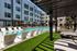 Pool deck with tanning loungers, turf lawn, shade pergola, and daybeds below apartment balconies