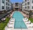 Courtyard lap pool with lounge chairs on turf, shade pergolas, string lights, and apartment balconies