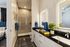 Bathroom with double vanity, lighted mirrors, tiled walk in shower, and dark countertop