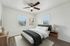 Bright and cozy bedroom with modern ceiling fan, plush bedding, natural light from dual windows, and elegant wooden furniture.