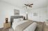 Bright and modern bedroom with cozy bedding, elegant wooden furniture, and stylish artwork. Features a ceiling fan for added comfort.