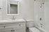 Elegant white bathroom featuring a sleek vanity with a modern faucet, a large mirror, and a pristine bathtub.