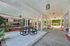 Charming outdoor patio area with stylish seating under a covered walkway, surrounded by lush greenery and vibrant landscaping.
