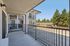 Expansive apartment balcony with sleek railings, offering a tranquil view of lush green trees and clear blue skies.