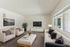 Inviting living room with modern decor, featuring a comfortable sofa, elegant armchairs, a large flat-screen TV, and abundant natural light from expansive windows.