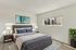 Elegant and spacious bedroom featuring a modern bed with plush bedding, flanked by stylish lamps, natural light streaming through large windows, and a vibrant potted plant adding a touch of greenery.