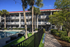 Charming apartment complex with stylish balconies, surrounded by lush greenery and palm trees, featuring an inviting pool area for ultimate relaxation.