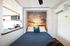 Cozy bedroom featuring a vibrant sunset mural, stylish bed with blue bedding, and compact modern kitchen area.