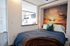 Cozy bedroom with sunset wall mural, adjacent to a modern kitchenette with sleek appliances.