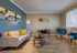 Contemporary living room with a cozy gray couch accented by yellow pillows, stylish blue chairs, and modern decorative elements on rich wood flooring.