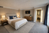 Elegant bedroom with a plush bed, cozy lighting, and modern decor. Large windows offer abundant natural light, complemented by a stylish dresser and a wall-mounted TV.
