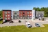 Modern apartment building with vibrant red and gray facade, ample parking space, and lush green surroundings.