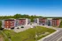 Modern apartment complex with vibrant red and gray facades, set against lush green trees and a clear blue sky, offering ample parking and inviting surroundings.