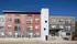 Modern apartment building with vibrant red and gray facade, spacious windows, and charming balcony railings under a clear blue sky.