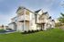 Charming duplex with elegant balconies, stylish siding, and manicured green lawn under a clear blue sky.