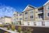 Modern apartment building with stylish beige siding and white trim, featuring balconies and spacious garages under a clear blue sky.