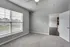 Bright, spacious room with soft carpet, large window, and a view of a cozy neighborhood, leading into a sleek open-concept living area.