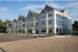 Charming three-story apartment building with classic architecture, featuring large windows and inviting balconies, all set against a backdrop of a clear blue sky.