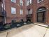 entrance to folcroft apartment building, colorful flowers in mulch bed, glass door leading into brick building with white windows, concrete walkway