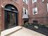 entrance to folcroft apartment building, colorful flowers in mulch bed, glass door leading into brick building with white windows, concrete walkway