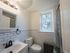 white bathroom with tile walls, vanity sink with cabinets, modern accents and energy-efficient toilet, window and shower curtain