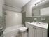 bathroom with tiled wall and shower, vanity sink, energy efficient toilet, steel accents